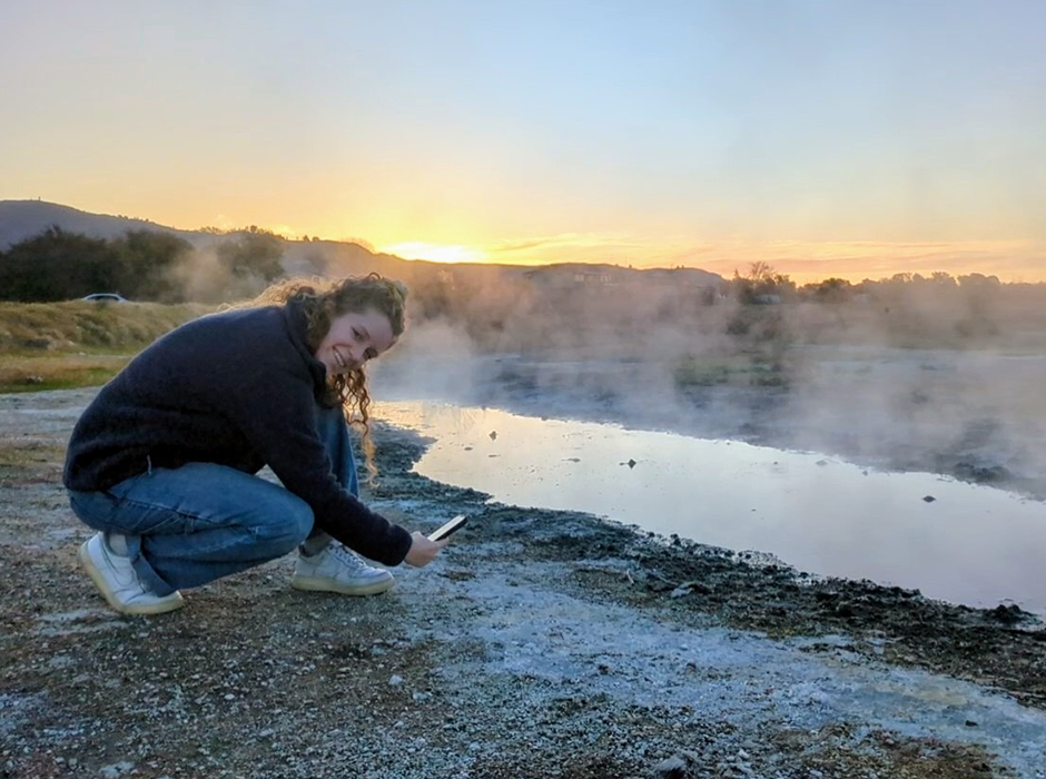 A women crouched on the ground by a steamy pool of water