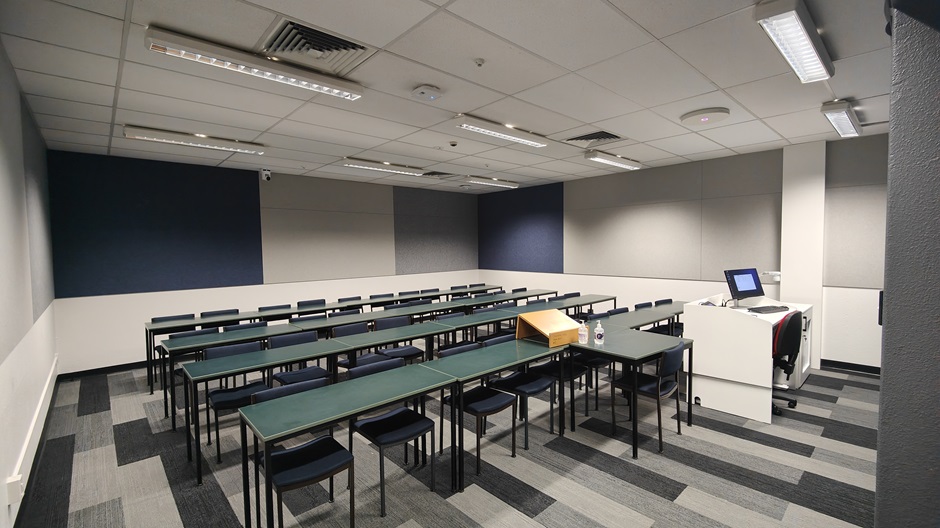 View of Burns 4 seminar room lefthand from front, with a computer on a lectern and tables and chairs in rows