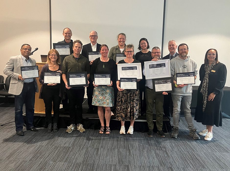 13 people standing in two rows, some holding certificates