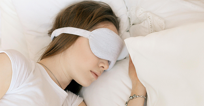 A woman wears an eye-mask and sleeps