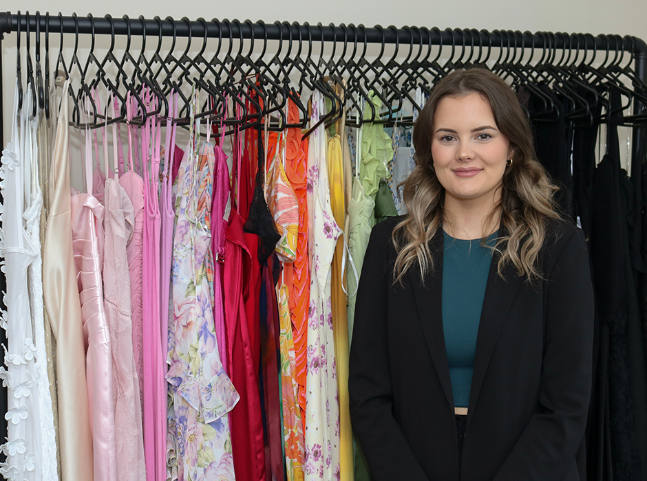 A woman standing next to a rack of dresses