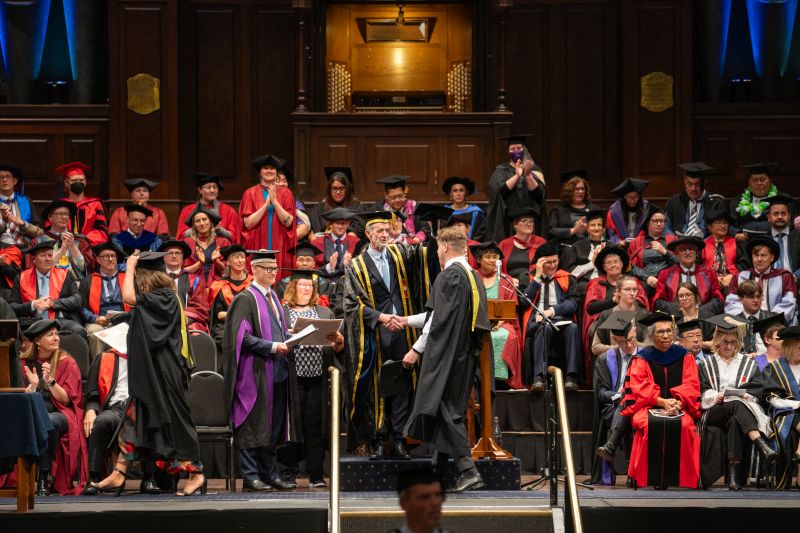 Graduation ceremony. University Chancellor shaking hands with graduating student