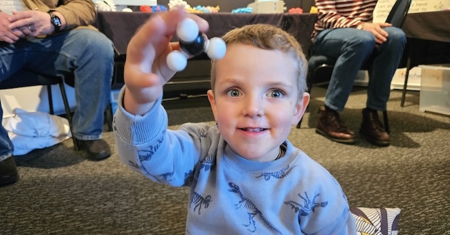 A small child holds up a plastic model of a molecule.
