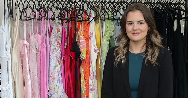 A woman standing next to a rack of dresses