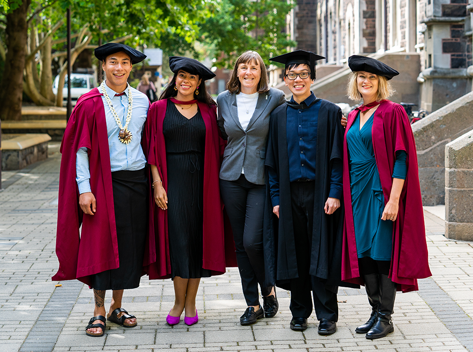 Five people standing, four in postgraduate gowns