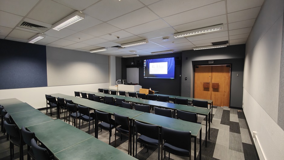 View of Burns 4 seminar room righthand from back, with tables and chairs in rows facing a projector screen