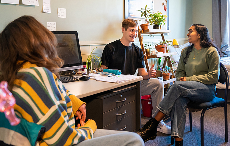 Three young people sitting in a bedroom, talking and laughing.