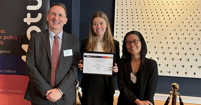 Amelia Farrar (centre) receiving her prize from Motu Executive Director John McDermott and Motu Senior Fellow Trinh Le.