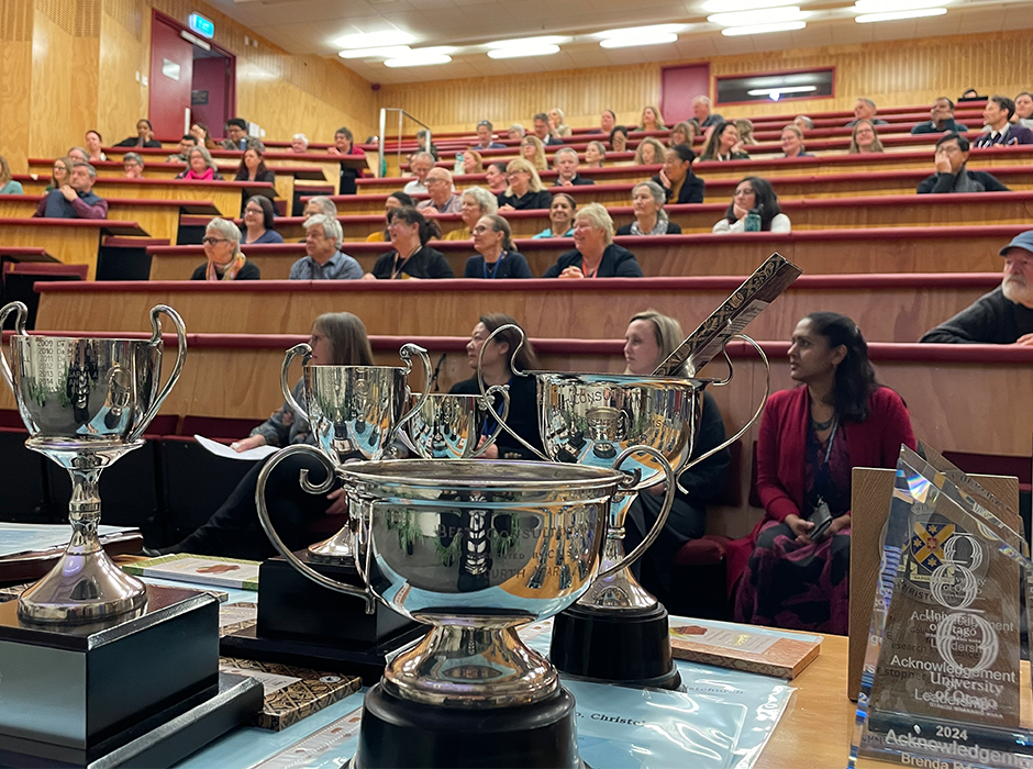 several awards on a table with people seated in a lecture theatre in the background