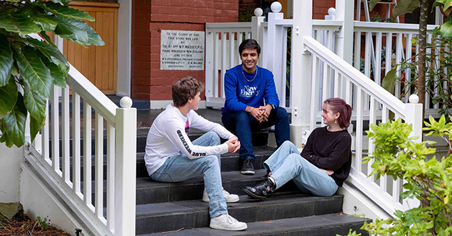 Three students sitting on the steps to the entrance of St Margaret's College.