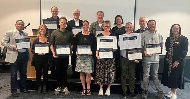 13 people standing in two rows, some holding certificates