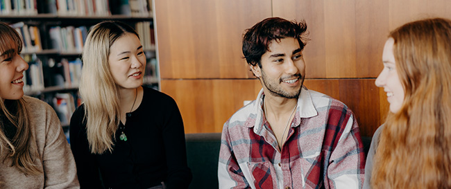 Four students talking and smiling in the University library