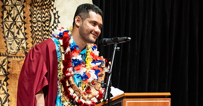 A man at a podium wearing many lei 