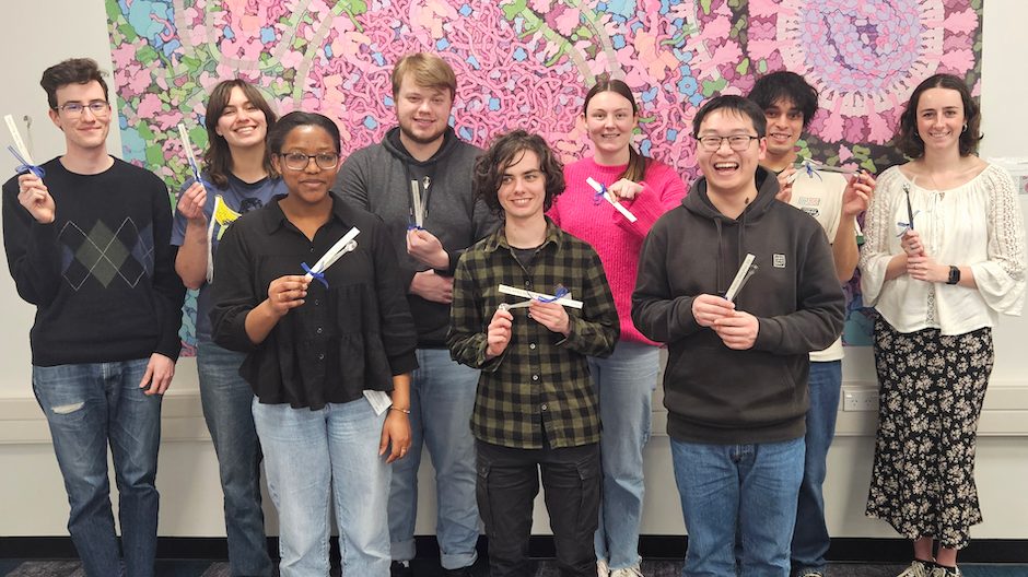 A group of standing, smiling students hold up little metal spatulas.