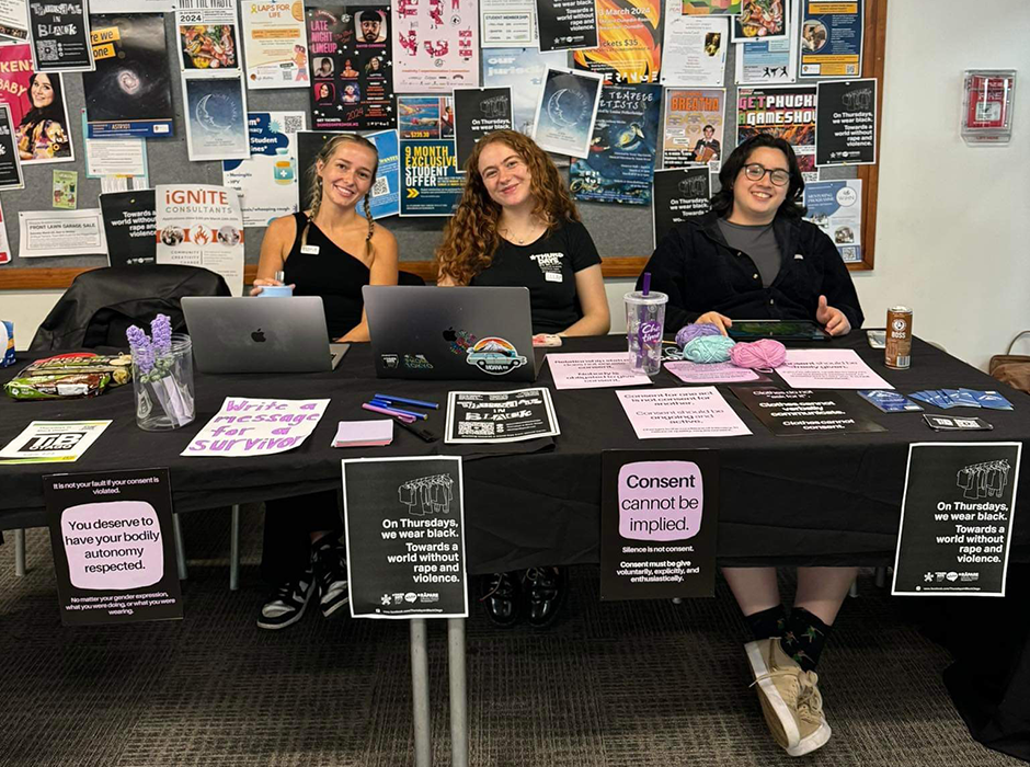 Three women sitting a desk with information to hand out