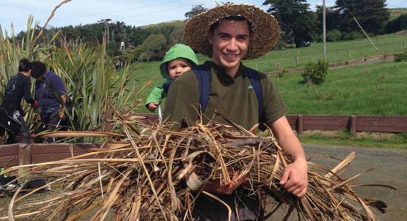 person carrying a baby on their back and some grasses in their arms