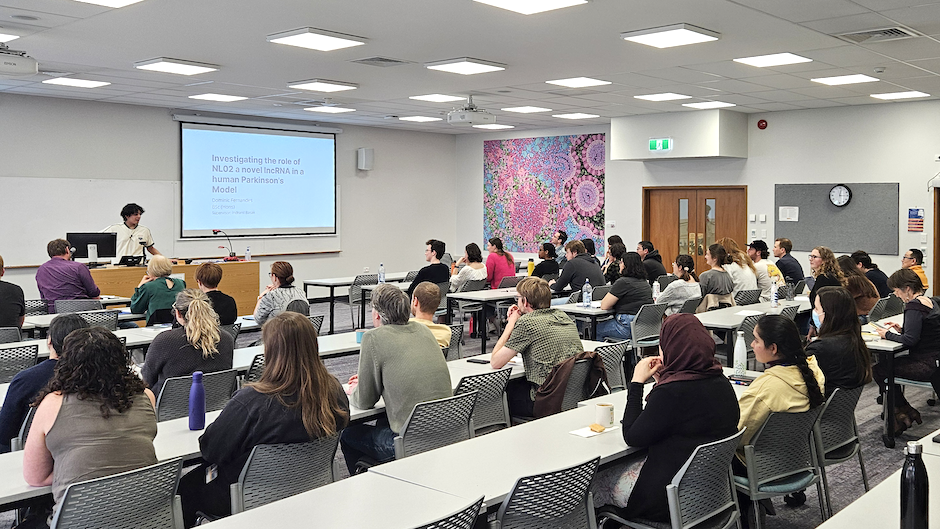 An attentive audience listens to a student talking at the front of the room.