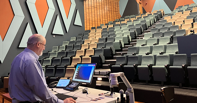 A man standing at the front of a lecture theatre 