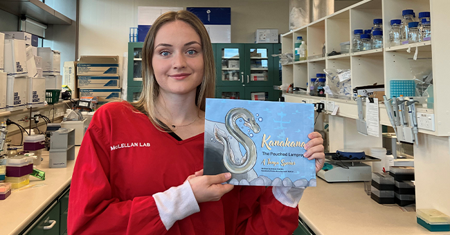 Biomedical Sciences graduate Ariana Drabble in the cancer immunotherapy lab with the book she wrote earlier this year on Kanakana, the pouched lamprey. 