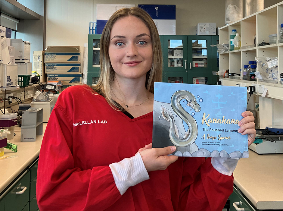 Biomedical Sciences graduate Ariana Drabble in the cancer immunotherapy lab with the book she wrote earlier this year on Kanakana, the pouched lamprey. 