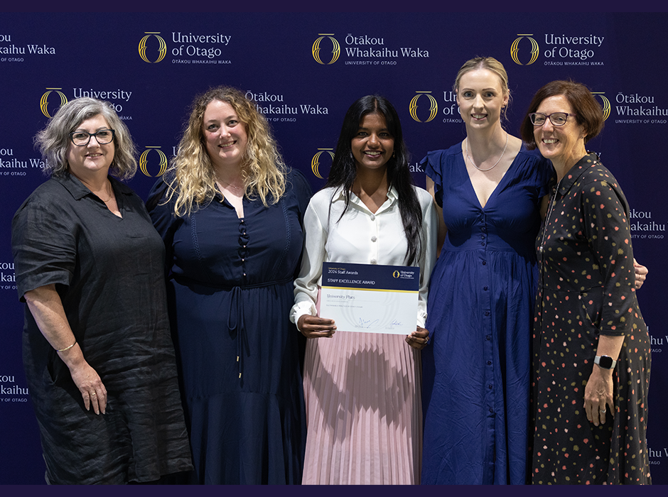 Five women standing on stage, the one in the middle holding the award