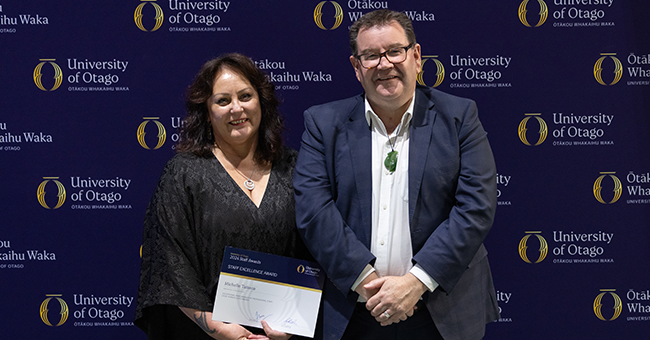 A woman on stage holding an award, standing next to a man 